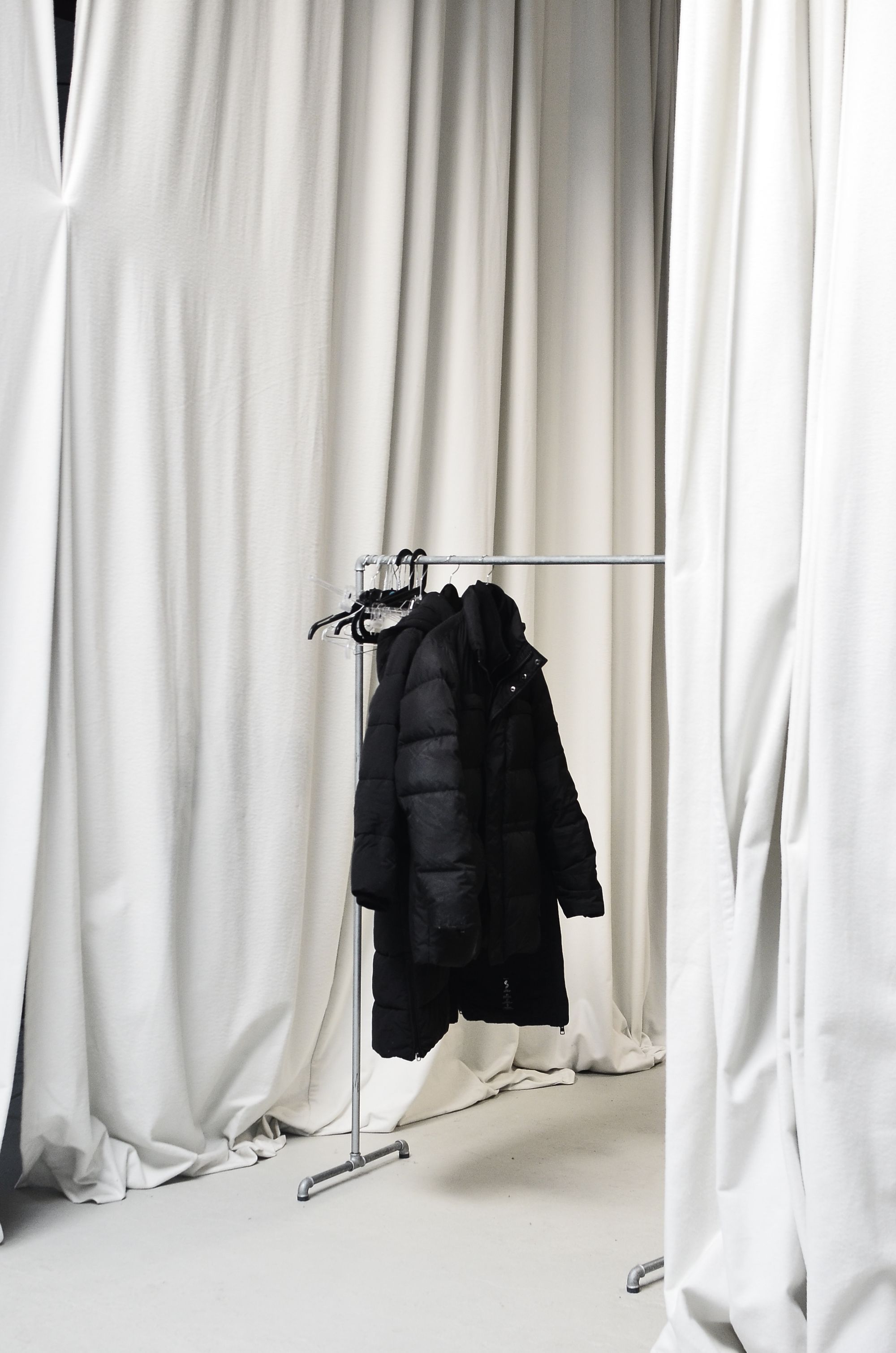 black down coat on a rail between white curtains